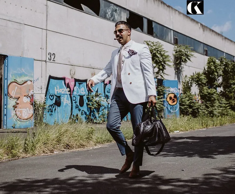 Ömer Kaya im weißen Sakko mit Ledertasche geht an einer Graffitiwand in Wiesbaden vorbei