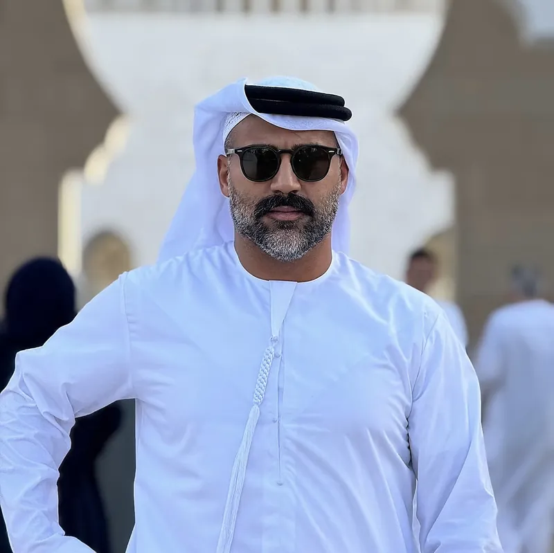Ömer Kaya im weißen Kandura mit Kopftuch und Sonnenbrille vor einer Moschee in Abu Dhabi