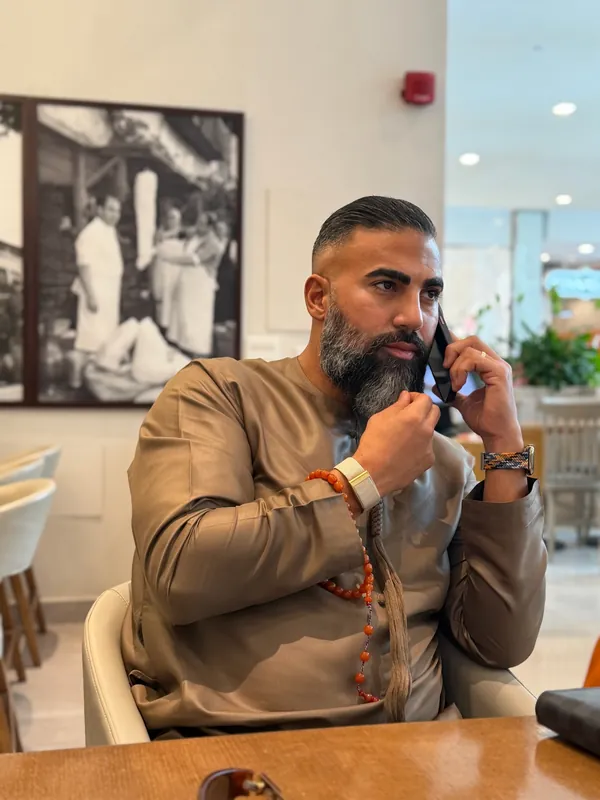 عمر كايا بكندورة بنية ومسبحة في يده يتحدث في الهاتف في مقهى في دبي