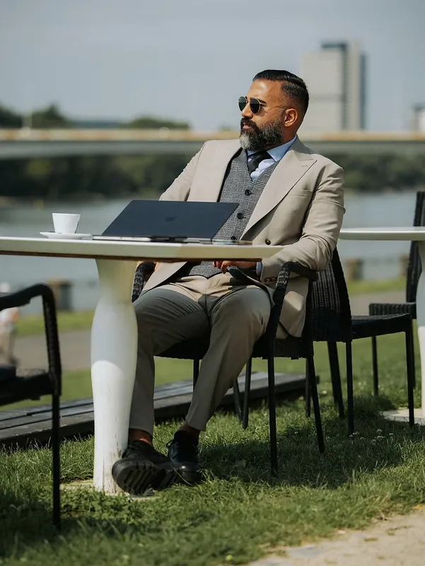 Ömer Kaya im beigen Anzug mit Laptop an einem Tisch am Wasser