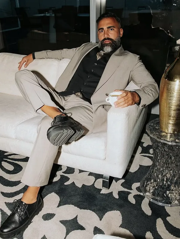 Ömer Kaya im beigen Anzug mit Kaffeetasse auf einem weißen Sofa in Dubai