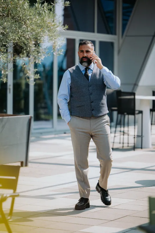 Ömer Kaya in Weste und heller Hose geht telefonierend über eine Terrasse